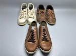 Lote composto por três pares de tênis masculinos usados. Primeiro par: marca Mr. Cat, cabedal em couro e camurça na cor bege/off-white, cadarço da mesma cor, sola em borracha clara, com etiqueta lateral identificada. Segundo par: cabedal em couro na cor marrom, cadarço marrom, sola em borracha. Terceiro par: cabedal em couro marrom com fechamento lateral por zíper e cadarço escuro, sola em borracha branca. Todos os pares apresentam sinais de uso. Numerações não identificadas nas imagens. sapatênis, sneaker, calçado esportivo, par de sapatos