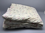 Cobre-leito matelassê em tecido de fundo creme, com estampa floral distribuída em toda a extensão da peça. O padrão apresenta rosas em tons de rosa e pink, folhagens em verde e pequenas flores azuis sobre hastes ramificadas. Costura matelassê em padrão ondulado, visível na segunda imagem. Medidas declaradas: 250 x 230 cm. Apresenta sinais de uso. colcha, edredom, coberta, cobertor decorativo, quilt, bedspread