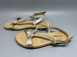 Par de sandálias rasteiras infantil, marca Bottero, com tiras em material sintético metalizado na cor dourada. Modelo com tiras cruzadas na parte frontal e alça traseira regulável com fivela dourada. Palmilha em material sintético na cor caramelo com logotipo da marca impresso. Solado plano em tom bege. Apresenta sinais de uso com desgaste nas tiras e na palmilha. Número não identificado nas imagens. calçado, sapatilha aberta, sandal, chinelo de tiras, flat