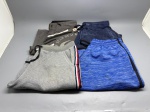 Lote composto por quatro peças masculinas: bermuda estilo boardshort em tecido cinza com estampa gráfica em preto e branco, cordão ajustável, botão frontal e bolso lateral com aba  visível logotipo parcial com referência a "Beach Fighter" e "Surfing Team"; calça de moletom cinza-mescla com detalhe de faixa lateral em vermelho e azul marinho; calça de moletom azul mesclado com faixa lateral preta; calça de moletom azul-marinho com aspecto delavê. Peças apresentam sinais de uso. Tamanhos não identificados nas imagens. short, bermudão, jogger, calça de academia, indumentária, conjunto