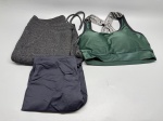 Lote composto por três peças de roupa esportiva feminina. A primeira é uma calça legging longa na cor preta, modelo saia-legging (skirt legging), com sobreposição de saia curta integrada na parte superior, cós largo dobrado. A segunda é uma calça legging cinza mescla dobrada, aparência de tecido com textura flame. A terceira peça é um top/sutiã esportivo na cor verde, com alças cruzadas nas costas e elástico com escrita estampada. Todas as peças aparentam uso. Tamanhos e marcas não identificados com precisão nas imagens. Estado de conservação a verificar. conjunto esportivo, roupa de ginástica, athleisure, sportswear, calça fitness, cropped esportivo, bralette