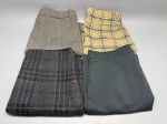 Lote composto por quatro saias femininas dobradas. A primeira, em tecido xadrez tom bege-acinzentado com fio branco, corte reto, fenda frontal e cós com fecho; a segunda, em tecido xadrez amarelo com listras pretas e brancas; a terceira, em tecido xadrez cinza-escuro com linhas marrons, aparência de lã; a quarta, em tecido liso verde-grafite com textura quadriculada sutil. Peças sem marca identificável nas imagens. Estado de conservação variável conforme a peça. Não há informações de tamanho ou composição de tecido visíveis. indumentária, roupa, conjunto de peças, saia reta, tartan, madras, mescla