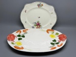 Lote composto por dois pratos em cerâmica esmaltada de fundo branco. O primeiro, de formato oval alongado, apresenta decoração pintada à mão com motivos de frutos do mar  caranguejos, camarões, rodelas de limão e ervas  distribuídos ao redor da borda, com relevos tridimensionais nas extremidades laterais representando caranguejos. O segundo, de formato quadrangular com borda recortada em ondas e filete cinza, é decorado com buquês florais policromicos dispersos. Ambos sem marcas de manufatura identificáveis nas imagens. Presença de pequenos sinais de uso. travessa, faiança, louça, peça de mesa, prato de serviço, majólica, earthenware