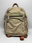 Mochila da marca Hedgren, confeccionada em nylon na cor bege com detalhes em tom verde oliva na faixa frontal. Apresenta logotipo da marca em metal prateado na frente, dois compartimentos com zíper na face frontal, zíper adicional na parte superior e alça de mão com revestimento em material sintético caramelo. Alças de ombro reguláveis em fita têxtil na cor caramelo. Puxadores de zíper com pingente metálico em formato quadrado com inicial  backpack, mochilinha, bolsa mochila, bag, sacola de costas