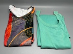 Lote composto por duas peças de roupa feminina. A primeira é uma regata em malha canelada na cor verde-água, com decote arredondado, alças largas e acabamento em ribana nas bordas; sem marca visível. A segunda peça é uma blusa ou top com estampa em sublimação, apresentando composição abstrata nas cores preto, vermelho, laranja e amarelo, com decote redondo e etiqueta interna parcialmente visível. Ambas as peças encontram-se dobradas e aparentemente em bom estado de conservação. Marca, tamanho e composição de tecido não identificáveis nas imagens. camiseta, top, camisa, peça de malha, indumentária, roupa, confecção