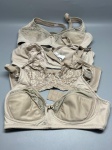 Lote composto por cinco sutiãs femininos na tonalidade bege/nude. As peças apresentam modelos variados: com aros, alças ajustáveis e fechamento traseiro por colchetes. Uma das peças possui copa em renda floral. Outra apresenta copa estruturada em tecido liso com bordado sutil na região central. As demais são em tecido liso com acabamento em ponto zigzag nas bordas. Uma das peças possui etiqueta de identificação presa à alça. Estado de conservação variável entre as peças. Marcas, tamanhos e composição de tecido não identificáveis com precisão pelas imagens. roupa íntima, peça íntima, underwear, corpete, soutien, busto, conjunto íntimo
