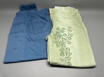 Lote composto por duas calças femininas. A primeira, na cor azul, confeccionada em tecido tipo sarja ou brim, com cós elástico, bolso traseiro e costura central nas pernas. A segunda, na cor verde-claro, em tecido similar, com cós e fechamento frontal por botão, bolsos traseiros e estampa floral em tons de verde ao longo da perna. Ambas dobradas, sem marcas visíveis identificadas nas imagens. Estado de conservação aparente: usado. pants, trousers, indumentária, peças do vestuário, conjunto de calças