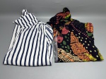 Lote composto por dois vestidos femininos. O primeiro, em tecido de algodão aparente, estampado em listras verticais azul-marinho e branco, com botões frontais e decote assimétrico de um ombro só. O segundo, em tecido leve provável viscose, estampado em fundo preto com motivos coloridos de elementos abstratos, estrelas amarelas, formas orgânicas em laranja, rosa, verde e amarelo; possui gola colarinho, manga curta e fechamento frontal por botões. Ambas as peças apresentam estado de conservação aparente sem danos visíveis. Marca e tamanho não identificados nas imagens. indumentária, roupa, peça de roupa, traje, veste, chemise dress, shirtdress
