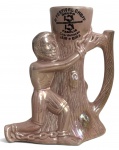 Caneca escultórica em cerâmica, decorada em esmaltação iridescente, representando figura masculina abraçada a tronco de árvore, com alça em formato de galho. Apresenta inscrição alusiva ao 4º FESTIVAL CHOPP  GRUPO FAMÍLIA, coordenação Jair e Bira. Peça decorativa e colecionável. Possui registro e numeração na base. Mede 19 x 18 cm.