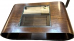 JORGE ZALZUPIN- Elegante Mesa de centro em madeira nobre laminado, com vidro, apresenta selo da L'Atelier. Med. 32 X 120 X 73 cm.(Não possui certificado, somente NF de arrematação).ZALSZUPIN, Jorge - Varsóvia, Polônia (1922) - Jorge Zalszupin nasceu em Varsóvia, Polônia, em 1922. Formou-se arquiteto na Romênia em 1945. Sua importância para o design brasileiro merece pesquisa, ainda não realizada. Além de ter sido dono da fábrica de móveis l'Atelier, de móveis modernos, Zalszupin liderou uma iniciativa ímpar: coordenou uma equipe de designers que trabalhavam para quatro distintas fábricas de um mesmo grupo empresarial, o grupo Forsa. Esta é uma experiência rara e talvez única no mundo.Zalszupin imigrou para o Brasil em 1949 e, depois de uma breve estadia na capital da República, estabeleceu-se em São Paulo, cidade que entrava num ciclo de grande crescimento industrial e de grandes transformações culturais. Abriu escritório de arquitetura , tendo como sócio José Gugliota, na primeira metade dos anos 1950. Ao cansar-se de projetar e mandar fabricar móveis exclusivos para as residências de seus clientes, decidiu associar-se a um grupo de marceneiros e produzir pequenas séries. Assim surgiu a fábrica l'Atelier, que logo começou a fabricar móveis de escritórios e que passou de uma marcenaria de procedimentos artesanais a uma indústria com produção seriada. A primeira peça desta série foi feita em 1959 e é uma poltrona apelidada de 'Dinamarquesa' pelos funcionários. Construída de jacarandá e estofada, e ela tem pés palito e o desenho de seus braços e pés frontais lembram as colunas projetadas por Niemeyer para o Palácio do Alvorada.No começo dos anos 1970, com sérios problemas financeiros, l'Atelier foi vendida para um grupo empresarial, que já era proprietário da Laminação Brasil (ferragens), da indústria de produtos plásticos Hevea e da fábrica de computadores Labo. A venda foi negociada com o 'passe' de Zalszupin como diretor de pesquisa e desenvolvimento de produtos. Desse modo, Zalszupin ampliou a equipe de designers - que já contava com Oswaldo Mellone - incorporando Paulo Jorge Pedreira e Lílian Weimberg, de forma permanente. Os designers batizaram o grupo empresarial de Forsa e passaram a atuar como laboratório de criação.As possibilidades técnicas oferecidas por quatro distintas plantas industriais foram potencializadas pela equipe de designers. Desta forma, a Hevea, que produzia commodities plásticas, ganhou uma linha de produtos muito sofisticada no desenho e firmou uma marca, a Eva, de utensílios domésticos, vendida em supermercados. A própria l'Atelier passou a usar o plástico injetado, produzindo painéis divisórios para escritórios e licenciando a cadeira de concha de polipropileno Hille desenhada por Robin Day. Além dos produtos que foram ao mercado, a equipe de design do grupo Forsa testou dezenas de novas idéias, que formam extraordinário acervo a ser pesquisado e que, certamente, muito influíram na base de atuação de Oswaldo Mellone e de Paulo Jorge Pedreira.A crise dos anos 1980 afetou profundamente o desempenho das empresas do grupo Forsa. A equipe de design se dissolveu no final da década. Oswaldo Mellone e Paulo Jorge Pedreira abriram seus escritórios individuais e Jorge Zalszupin dedicou-se exclusivamente a arquitetura, atividade que nunca abandonara.A partir de 2005, a empresa Etel Marcenaria passou a produzir vários dos itens projetados por Zalszupin para l'Atelier - entre eles a poltrona 'Dinamarquesa' - , privilegiando os objetos da fase artesanal da empresa.