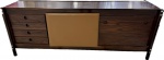 Sergio Rodrigues  - Magnífico Buffet em jacarandá com duas portas, detalhe em uma das portas em couro natural, detalhes em metal cromado, 4 gavetas na lateral esquerda, parte interna com prateleira. Med. 76 X 202 X 50 cm. (peça em perito estado, Não possui certificado, vai com NF de arrematação).  Nota: Sérgio Rodrigues (Rio de Janeiro (RJ), 22 de setembro de 1927 Rio de Janeiro (RJ), 1 de setembro de 2014). Foi um arquiteto e designer brasileiro. Junto com Joaquim Tenreiro e José Zanine Caldas, foi o pioneiro a transformar o design brasileiro em design industrial e torná-lo conhecido mundialmente.Iniciou seu trabalho na arquitetura no projeto do Centro Cívico de Curitiba junto com os também arquitetos David Xavier de Azambuja, Flávio Régis do Nascimento e Olavo Redig de Campos.Teve o auge da sua carreira nos anos 50 e 60. Trabalhou com design de móveis de acordo com o modernismo no Brasil, trazendo a identidade brasileira para seus projetos tanto nos desenhos, quanto nos materiais tradicionais couro, palhinha e madeira - exaltando a cultura brasileira e indígena."De fato, nesse momento ele fez coexistir o Brasil-brasileiro com o Brasil-de-Ipanema, cantada mais tarde (1962) por Tom Jobim e Vinicius de Morais na célebre "Garota de Ipanema"(Oscar Niemeyer).Contemporâneo de Oscar Niemeyer e Lúcio Costa, seu mobiliário foi utilizado em larga escala na construção da capital brasileira Brasília."Naquela época (início de Brasília) não se tinha tempo de pensar em desenhar móvel nenhum. Nós usamos móveis correntes no mercado, selecionando como o Palácio exigia. O principal designer a quem solicitei móveis foi Sérgio Rodrigues." (Lúcio Costa).Seu trabalho mais famoso é a poltrona mole de 1957, feita em couro e madeira com inovações de encaixe e estofado que inspiram produtos até hoje. Atualmente, a poltrona Mole integra o acervo do Museu de Arte Moderna (Nova Iorque) (MoMA).O móvel não é só a figura, a peça, não é só o material de que esta peça é composta, e sim alguma coisa que tem dentro dela. É o espírito da peça. É o espírito brasileiro. É o móvel brasileiro. (Sérgio Rodrigues).Ele faleceu na manhã da segunda-feira (1 de setembro de 2014). De acordo com uma das funcionárias do escritório do designer, Sérgio já apresentava um quadro de saúde debilitado há alguns dias. O motivo da morte não foi divulgado.