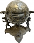 Antigo Porta Caviar em Pilter ricamente decorado com figuras de Querubins e Cachorro e globo com figuras florais, apresenta perda de banho de prata, marcas do tempo, no estado. Med. 23 X 22 cm.