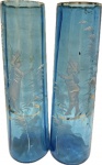 MARY GREGORY - USA - Séc. XIX/XX - Elegante par de Vasos em vidro artístico de tonalidade azul ricamente decorado com pintura esmaltada Representando "Casal no Jardim". Med. 24 X 7,5 cm. NOTA: Mary Gregory (1856-1908) foi uma artista russa que viveu nos Estados Unidos. Aprendeu a técnica de pintura com esmalte em vidro na Bohemia e essa técnica a tornou reconhecida levando a criação de uma empresa denominada Sandwich Glass Company em Cape Cod, Massachusetts. Ela foi especialmente bem conhecida por suas pinturas de crianças da era Vitoriana e tais obras de arte tem sido referidas como Mary Gregory desde 1920. O Westmoreland Glass Company de Grapeville, Pennsylvania começou a comercializar seu trabalho em vidro como Mary Gregory na década de 1920. Eles iriam criar pinturas de vidro com perfis de crianças da era Vitoriana como a artista fazia, e diziam que foi feito no estilo de Mary Gregory. Gregory, sua irmã, e, possivelmente, outros que ela tinha treinado, usaram uma tinta de esmalte branco e vidro moído em sua decoração. Para vincular a tinta ao vidro, após a aplicação ele era fundido com a peça, dessa maneira a pintura tornava-se parte do vidro.