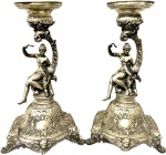 WMF - Germany - Séc. XIX - Excepcional Par de Castiçais em Metal Espessurado a Prata, Ricamente Decorado com Figura Central de Ninfa com Querubim, Base trabalhada com figuras florais, folhagens e rostos, peças assinadas. Med. 36 X 20 X 22 cm.