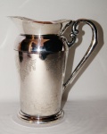 Espetacular jarra de água em metal espessurado a prata com belíssima alça e ricas gravações de guirlandas e volutas. Medida 22 cm de altura.