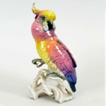 Cacatua em porcelana alemã Karls Ens Volksted, pousada sobre tronco com bela anatomia e fina plumagem nas cores azul, rosa e amarelo, c. 1920/30. Altura: 19,8 cm