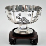 Bowl com pé em prata chinesa repuxada com personagens, aves e flores em relevo, contrastada no fundo. Peso 607 g. Meds: 18,0 cm (com a base), 13,0 cm x 19,0 cm (bowl)