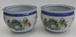 Par de `fish-bowls` (cachepôs) de porcelana oriental com fundo branco decorado com cenas festivas, policromadas, de casais orientais. Barrado azul. 30 cm de altura x 41 cm de diâmetro.