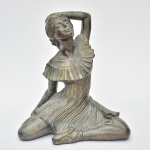 Linda escultura ao estilo art deco confeccionada em resina revestida em folha metálica representando "bailarina", pátina imitando bronze. Med.: 27x26x18 cm.