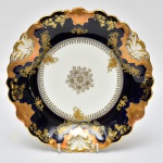 LIMOGES - Belíssimo e raro prato francês de coleção em porcelana do Séc. XIX, nas cores azul cobalto e branca apresentando riquíssima ornamentação floral em folha de ouro, borda recortada e decorada com concheados. Peça marcada na base. Med.: 23,5 cm.