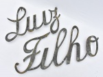 Letreiro escrito em bronze com o nome próprio "Luiz Filho". Med.: 33x108 cm.Obs: necessita solda entre as letras "i" e "l" no nome "Filho".
