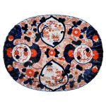 Travessa em porcelana japonesa IMARI, em formato oval levemente canelada com rica decoração de flores e elementos vegetais em rouge d fer e azul com grandes reservas, século XIX. Meds: 37,5 cm x 28,5 cm