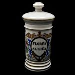 Pote de farmácia em porcelana com pintura de flores e serpentes reserva oval com inscrição `FLORES ALTHEA`. Altura: 29,0 cm