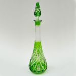 Garrafa em cristal da Bohemia com overlay verde, com belo relevo de pastilhas em desenhos geométricos, pescoço facetado de arestas serrilhadas. Altura: 47,0 cm