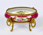 Covilhete com pés de origem francesa de porcelana e metal dourado, adornado por pintura floral em reserva Farta guarnição de metal estilo império.Cor predominante o Bordeaux. Marcas na base. Med. 9 cm de altura x 15 cm de diâmetro.  Marcas do tempo. No estado.