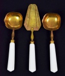 Conjunto de três talheres de servir em metal nobre dourado e cabos brancos. Sendo duas conchas para molhos e uma espátula. Medidas: Compr. 22,5 cm. (conchas) e Compr. 29,5 cm ( espátula ).