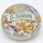 Peso para papel em cristal com flores no interior e a inscrição "S Simon". Med.: 5 x 8 cm.