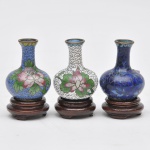 Três miniaturas de vasos chineses em metal com rico trabalho em cloisonné, sendo: branco, verde e azul com decoração floral. Base me madeira. Medindo 5 cm de altura sem a base e 6,5 cm de altura com a base.