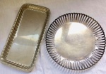 Par de travessas para petiscos, uma retangular, ass: Roberto Simões. Outra redonda com galeria vazada, contrastada. Metal prateado. Med. 22cm maior e 18cm menor.
