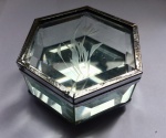 Linda caixinha porta joias em cristal bisotado, circundada por metal prateado, todo trabalhado. Lapidação representando flor. Fundo da caixa possui vidro. Suspensa por quatro pés. Med. 7x7 cm