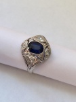 JOIA- Magnífico e antigo anel em platina, estilo art décor, ricamente cravejado por brilhantes ao redor de lindíssima pedra central em safira azul. Aro 18/19.
