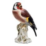 Escultura em porcelana alemã de pássaro pousado sobre tronco, marca da manufatura no fundo. Alt: 13,0 cm