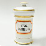Antigo pote de farmácia em porcelana francesa com inscrições UNG. HYDRARG. em reserva com faixa vermelha e faixas douradas na moldura, base e tampa.Altura 21,5 cm