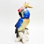 Grade cacatua em porcelana alemâ Karl Ens, Volksted, com bela anatômia e fina plumagem em relevo, policromia em azul, amarelo e rosa. Altura 35 cm.