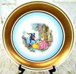 PRATO em porcelana esmatado na cor branca e vitrificado com elegante e larga faixa na borda em ouro velho. Ao centro pintura de cena romantica . Diâmetro 18,5 cm.