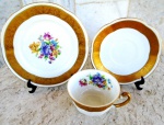 Trio de xícara para chá, com pires e prato para bolo em porcelana POLONESA com fundo branco esmaltado e vitrificado com ramos de flores do campo. Larga faixa em ouro em todas as peças. Medidas 10/15/17/cm.