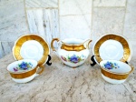 Tres peças : par de xícaras com pires e Cremeira /Leiteira em porcelana esmaltadas brancas e vitrificadas com ornamentação de buque de flores e largas faixas em ouro . medidas 7 /11 e cremeira 10/13 cm.