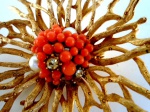 Grande broche em forma de sol com raios em metal dourado com banho de ouro e miolo com pequenas pedras na cor coral . Diâmetro 8 cm.