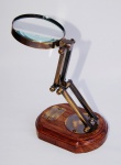 Belíssima lupa em bronze com base em madeira ostentando placa dizeres "Watkins & Hill Opticians -London- 1805". Medidas: 20 cm de altura e 8 cm de diâmetro de lente. Peça sem uso e na caixa original.