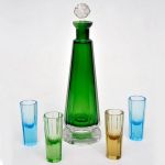 Licoreira em cristal europeu facetado na cor verde acompanha 4 copos multicoloridos. Alt: 26,0 cm (um copo com lascado e fundo da garrafa com trincado)