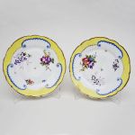 Par de pratos em porcelana inglesa decorada com pintura de flores, folhas e frutos com borda em faixa amarela e frisos dourados, marcada no fundo. Diam: 24,0 cm