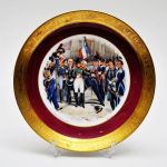 Medalhão em porcelana Epiag Royal tchecoslovaquia com cena de Napoleão `Les Adieux de Fontainebleau`, assinado Bongés, com faixa na cor vinho e faixa de personagens da mitologia gravadas a ouro em toda a borda. Diam: 26,0 cm
