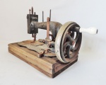 Antiga máquina de costura de funcionamento manual, sobre base de madeira. Apresenta desgastes do tempo. Medidas de 40cm x 19cm. No estado.
