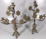 Par de candeladros de latão para três velas. Decoração floral, oriunda de vaso com alças sobre tripé. 50 cm de altura.