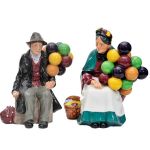 Pendant de esculturas em porcelana inglesa ROYAL DOULTON, representando casal de vendedores de balão, tituladas `The Baloon Man` e `The Old Baloon seller`. Alturas: 18 cm; 19 cm.