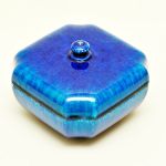 Caixa em cerâmica esmaltada de Sevres na cor azul irridescente em formato quadrado de cantos canelados. Medidas: 13,5 x 13,5 x 9,5 cm.